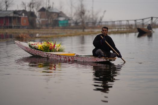 A man paddles a boat filled with vibrant flowers on a serene lake, showcasing a peaceful lifestyle.