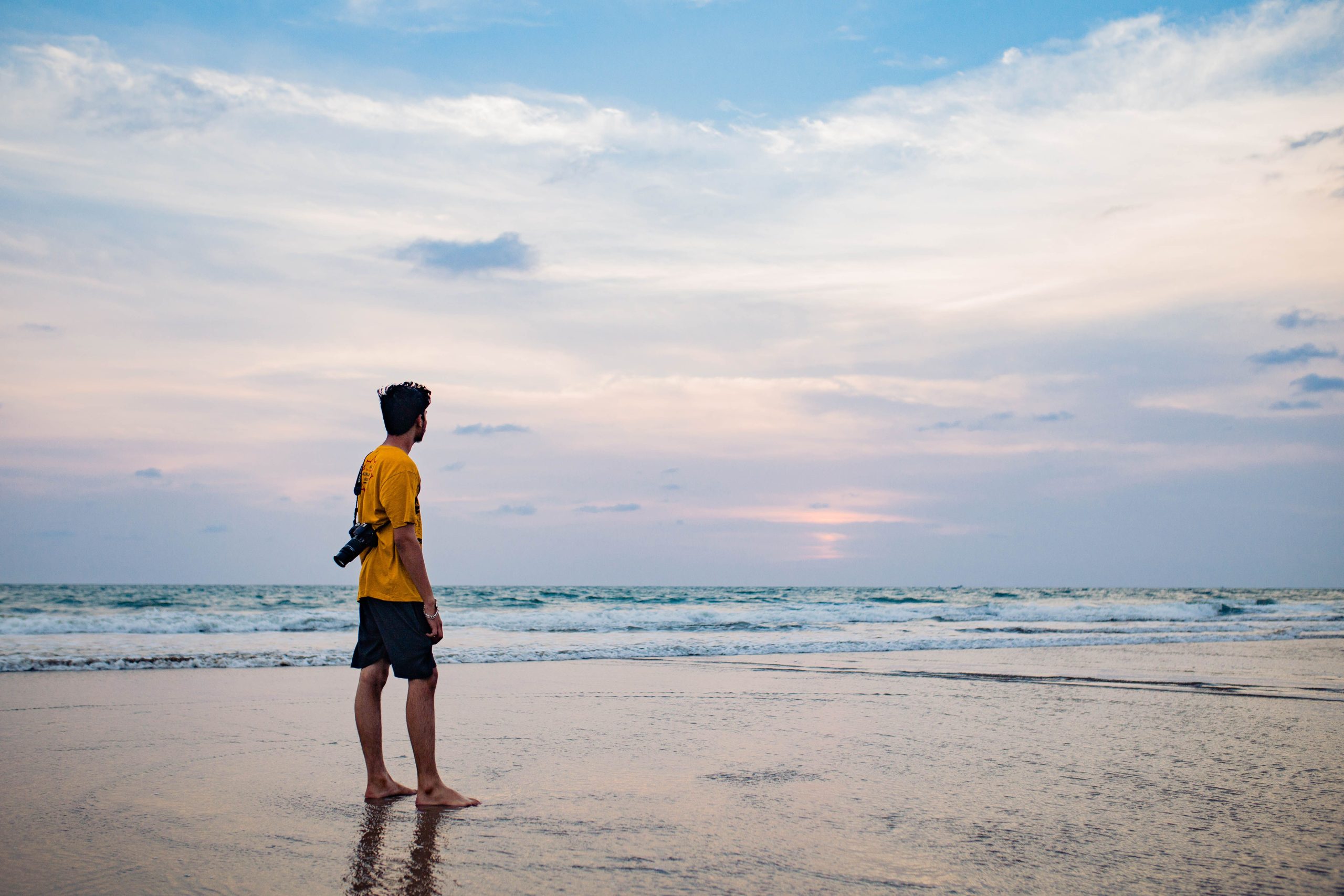 A man with a camera gazes at the serene sunset on a peaceful Goa beach, embracing tranquility.